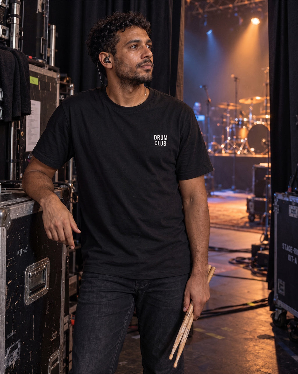Drummer wearing a black DRUM CLUB Classic Tee in a live performance or backstage setting.