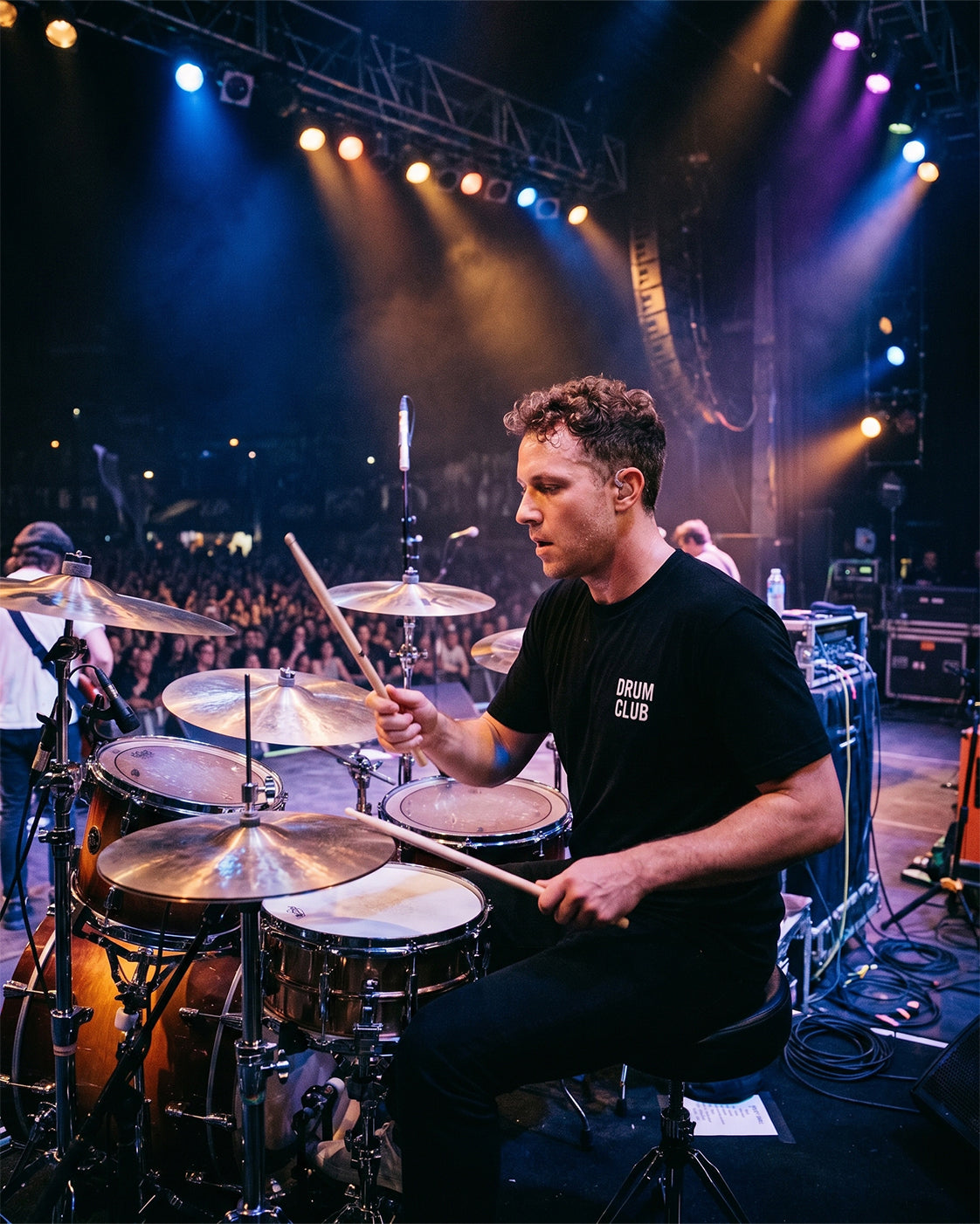 Drummer playing drums on stage during a live concert wearing the black DRUM CLUB Classic Tee with white chest logo.