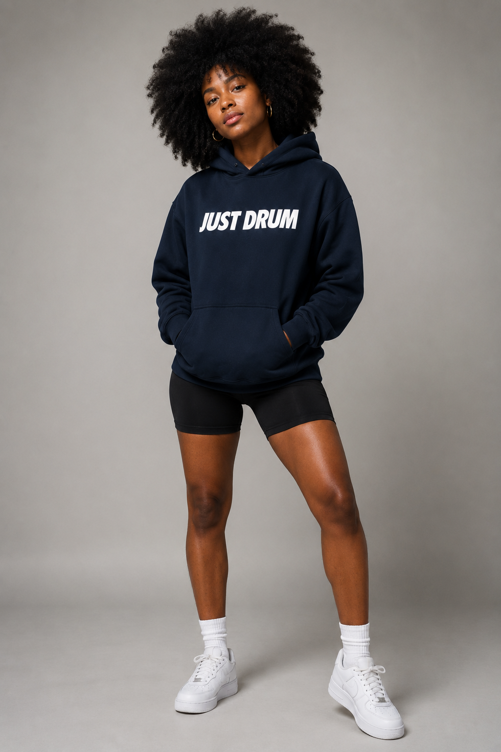 Black female model with afro wearing navy JUST DRUM hoodie in full-body studio portrait.